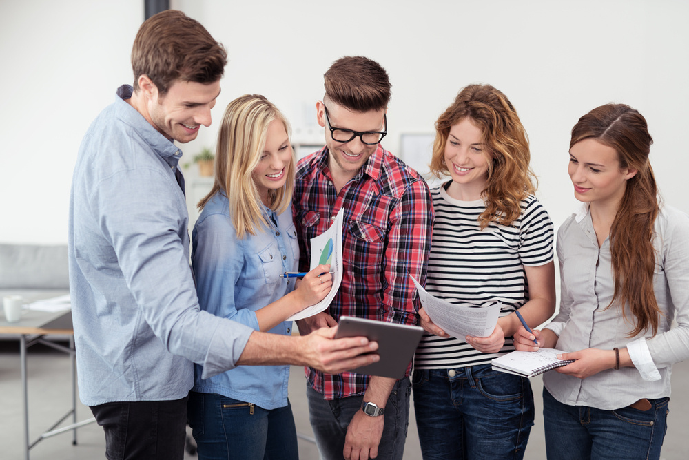 Three Quarter Shot of Five Young Office People Looking at the Tablet Screen Together with Happy Facial Expressions Inside the Office.